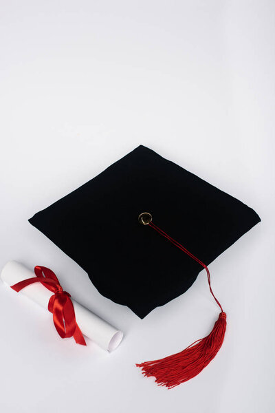 Black graduation cap with red tassel and diploma on white background