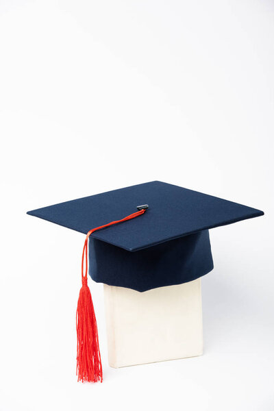 Blue graduation cap with red tassel on book on white background