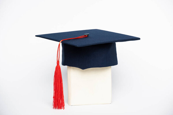 Graduation cap with red tassel on book on white background