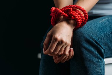 Cropped view of victim hands tied with rope isolated on black clipart