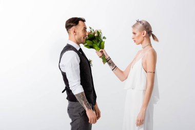 Güzel dövmeli gelinin yan görüntüsü beyaz tenli yakışıklı damat buketi ile vuruyor.