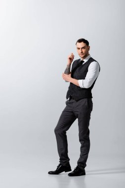 Yakışıklı dövmeli zarif damat gri arka planda poz veriyor.