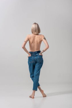 Gri cebinde elleri olan seksi, üstsüz, dövmeli bir kadın.