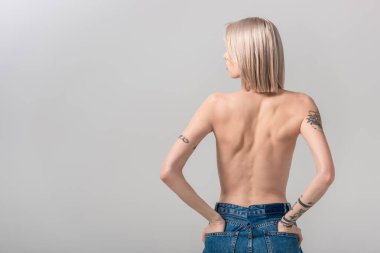 Gri renkli cepleri olan seksi, üstsüz, dövmeli bir kadının arka plan görüntüsü.