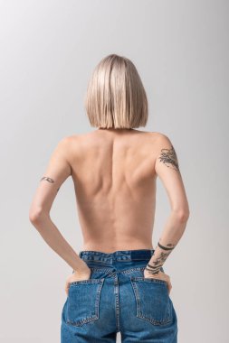 Gri renkli cepleri olan seksi, üstsüz, dövmeli bir kadının arka plan görüntüsü.