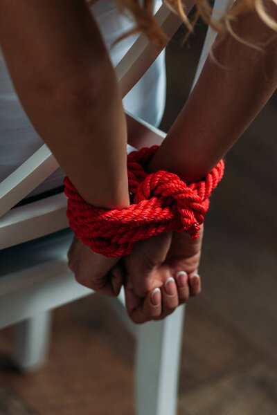 Cropped view of female hands tied with red rope on wooden background