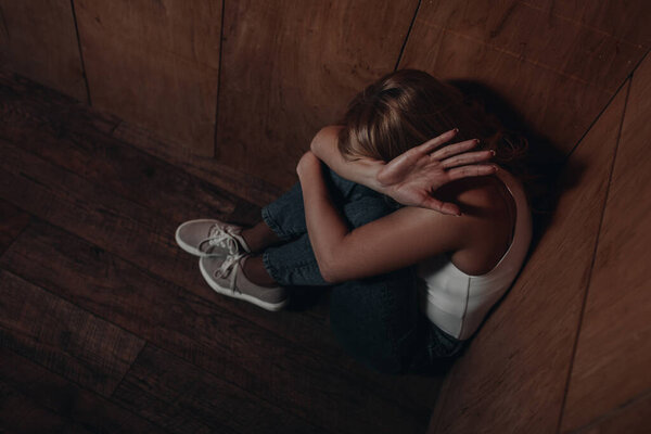 High angle view of victim with obscure face showing stop and sitting in corner