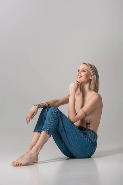 Feliz Jovem Topless Tatuado Menina Jeans Sentado Chão Fundo Cinza — Fotografia de Stock