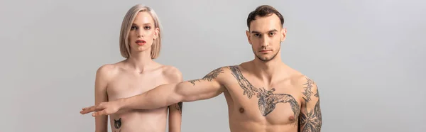 young naked tattooed couple isolated on grey, panoramic shot