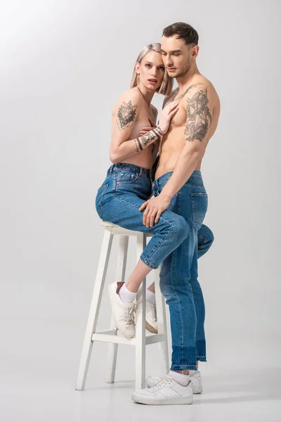 Jovem Sem Camisa Tatuado Casal Jeans Abraçando Cadeira Cinza — Fotografia de Stock