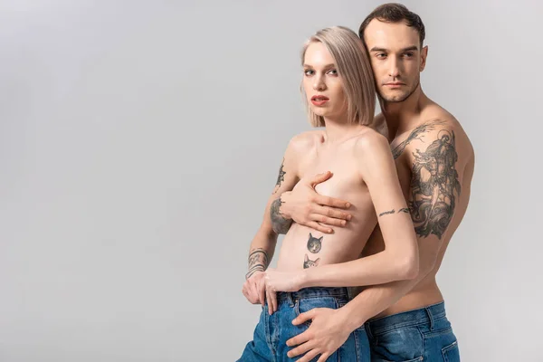 Jovem Sem Camisa Tatuado Casal Jeans Abraçando Isolado Cinza — Fotografia de Stock