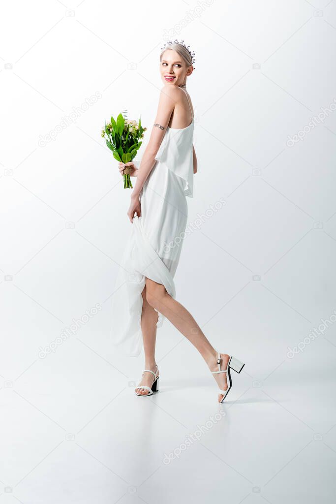 smiling beautiful tattooed bride with posing bouquet on white
