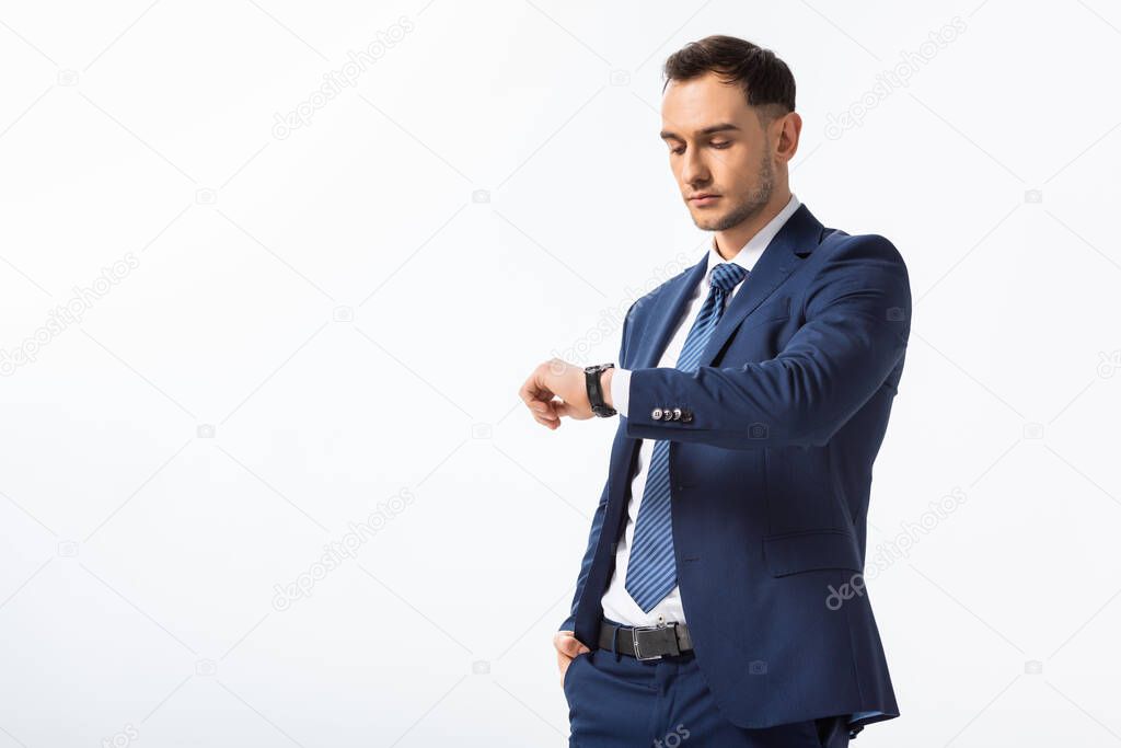 successful young businessman in blue suit looking at wristwatch isolated on white