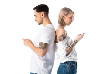 Genç dövmeli çift akıllı telefon kullanıyor. Sırt sırta durarak beyazları izole ediyorlar.