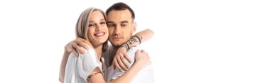Mutlu, genç, dövmeli çift sarılıyor, beyaz panoramik çekimde izole edilmiş.