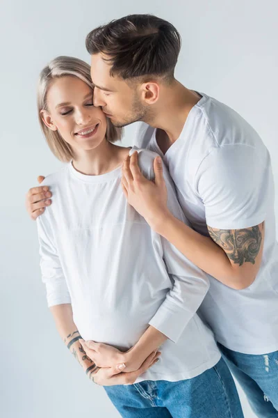 年轻纹身孕妇亲吻与丈夫隔离在灰色 — 图库照片