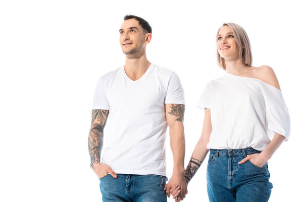 smiling young tattooed couple holding hands isolated on white