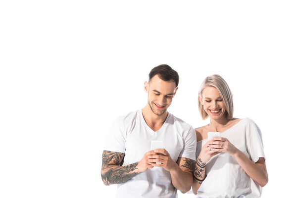улыбающаяся молодая татуированная пара с помощью смартфонов, изолированных на белом
