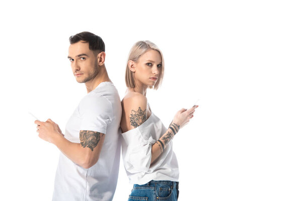 молодая татуированная пара с помощью смартфонов, стоя спиной к спине изолированы на белом
