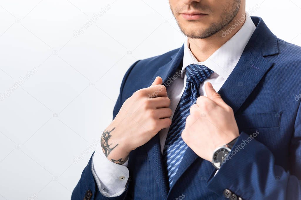 cropped view of successful tattooed businessman in blue suit with hands on blazer isolated on white