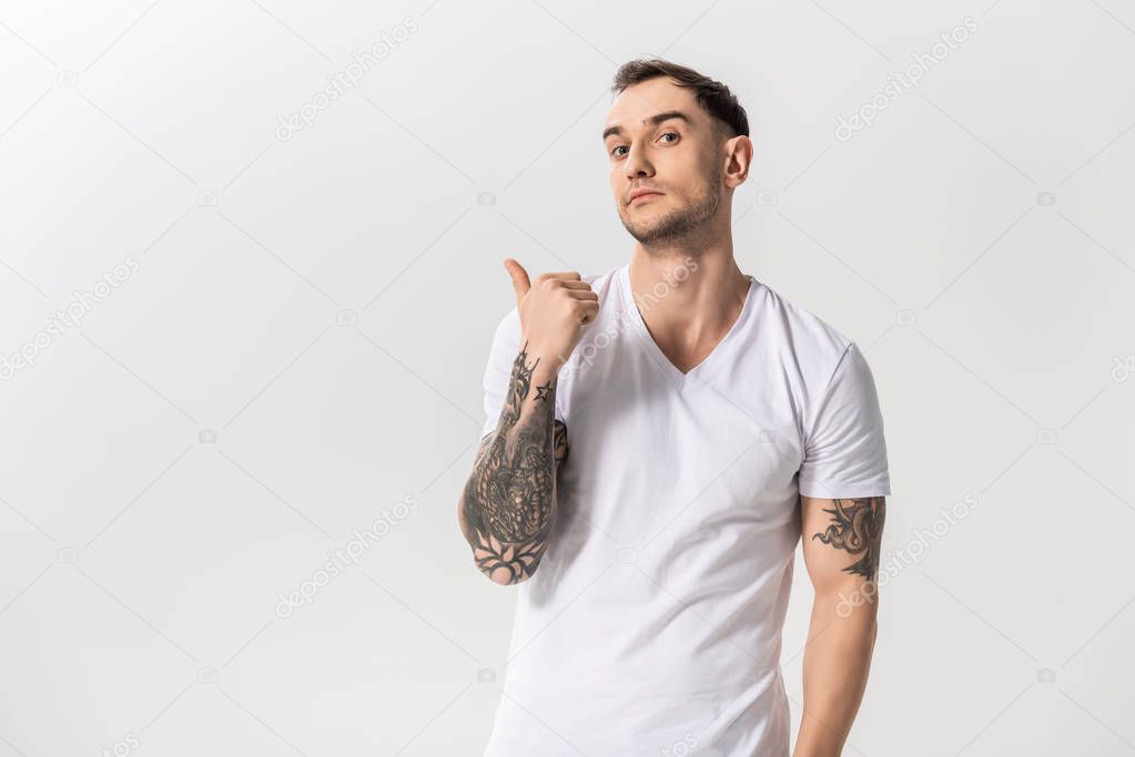 handsome young tattooed man pointing with finger aside isolated on white