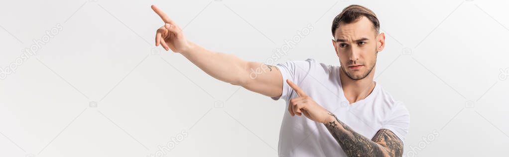 handsome young tattooed man pointing with fingers aside isolated on white, panoramic shot