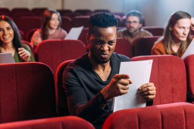 Kızgın Afrikalı Amerikalı aktör oyuncularla kırmızı sandalyelerde prova yapıyor.