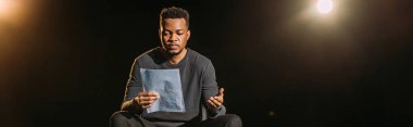 panoramic shot of african american actor holding scenario on stage during rehearse  clipart