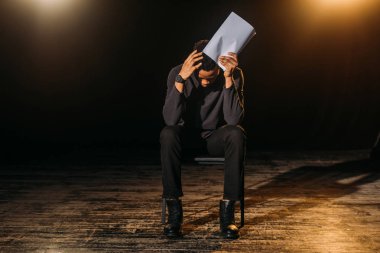Stresli Afrikalı Amerikalı aktör prova sırasında sahnede senaryo tutuyor 