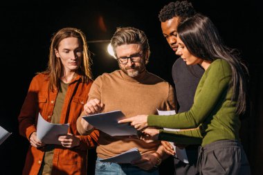 theater director, multicultural actors and actress rehearsing with scripts on stage clipart