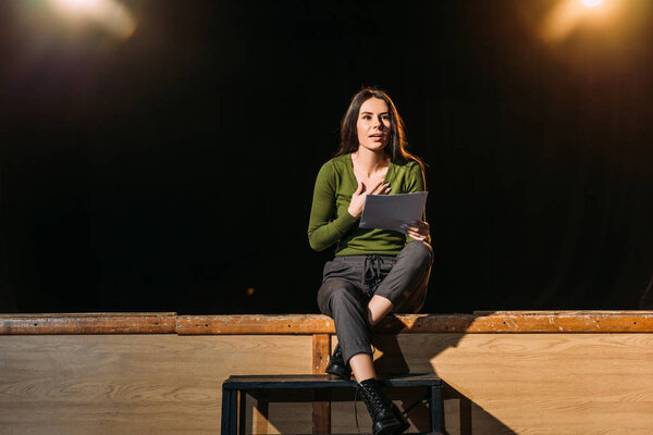 actress performing role with screenplay on stage in theatre