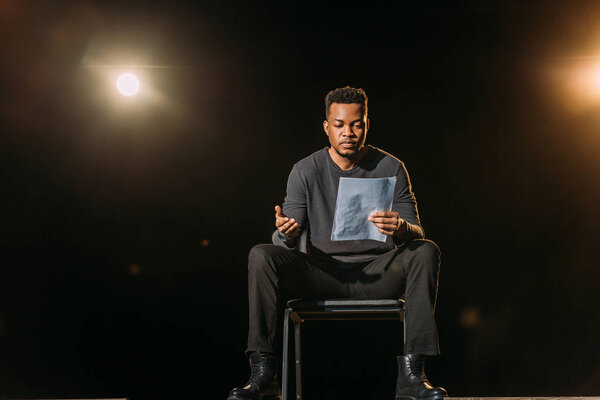 handsome african american actor holding scenario on stage during rehearse 
