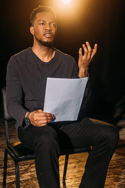 handsome african american actor holding scenario on stage during rehearse 