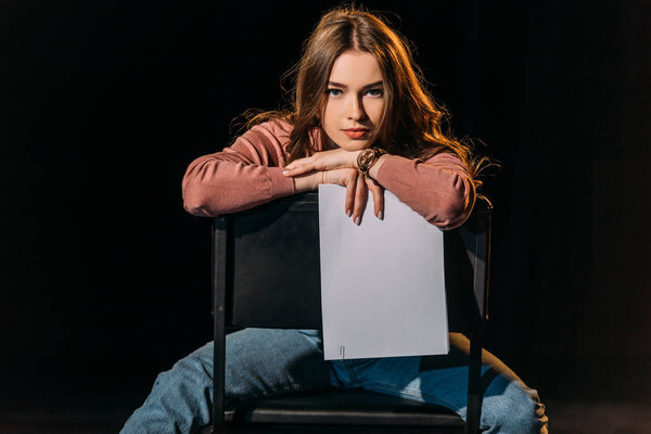 attractive young actress with scenario sitting on chair on stage in theatre