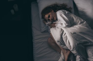 Yatakta yatan gecelikli şeytani takıntılı kadının üst görüntüsü.