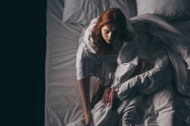 Şeytani paranormal kadın, geceliğiyle yatakta oturuyor.