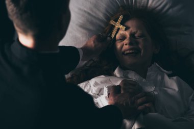 exorcist holding cross over laughing demon in bed clipart