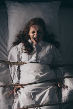 demonic obsessed yelling girl in nightgown bound with rope in bed clipart