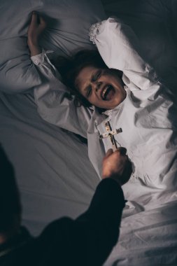 Şeytan çıkarıcı yatakta korkunç bir iblisin üzerinde haç tutuyor.