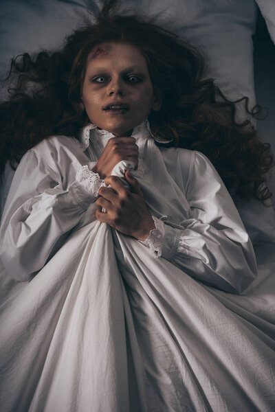 Вид сверху на демоническую девочку в ночном халате, лежащую в постели
