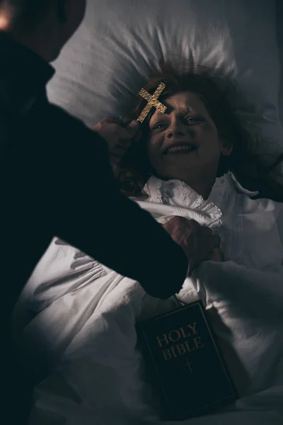 Exorcista Com Bíblia Cruz Sobre Menina Demoníaca Cama — Fotografia de Stock