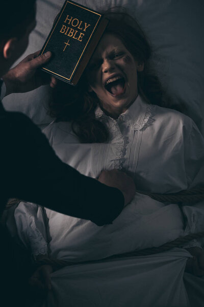экзорцист с библейской и одержимой кричащей женщиной в спальне
 