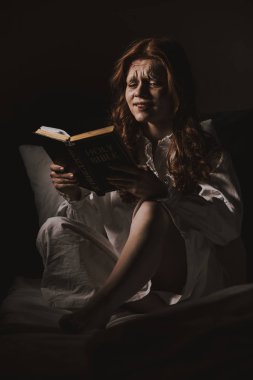 Yatakta kutsal kitap okuyan gecelikli, ağlayan şeytani kadın.