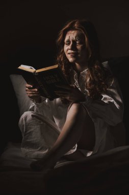 demonic crying woman in nightgown reading holy bible on bed clipart
