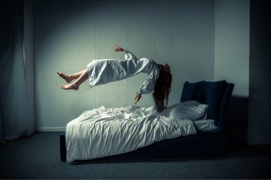 Gecelikli ürkünç kadın uyuyor ve yatağın üzerinde uçuyor.