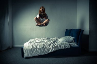 creepy smiling girl in nightgown levitating over bed while reading bible clipart