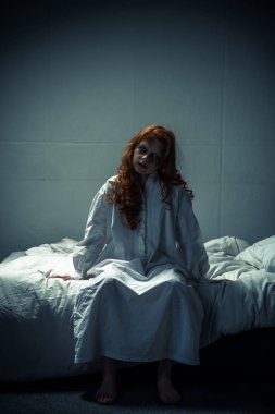 Yatakta oturan gecelikli ürkünç şeytani kadın.