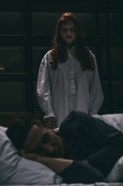 Yatağın yanında uyuyan adamla duran saplantılı kız.