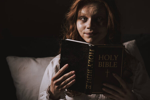 creepy demoniacal girl in nightgown holding holy bible 