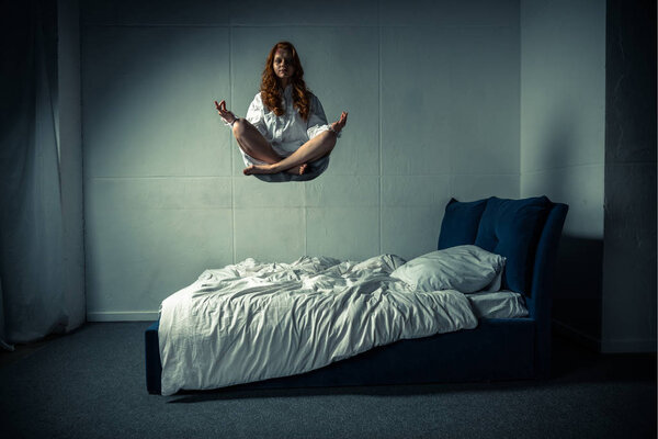 одержимая девушка, левитирующая в позе лотоса во время медитации над кроватью
